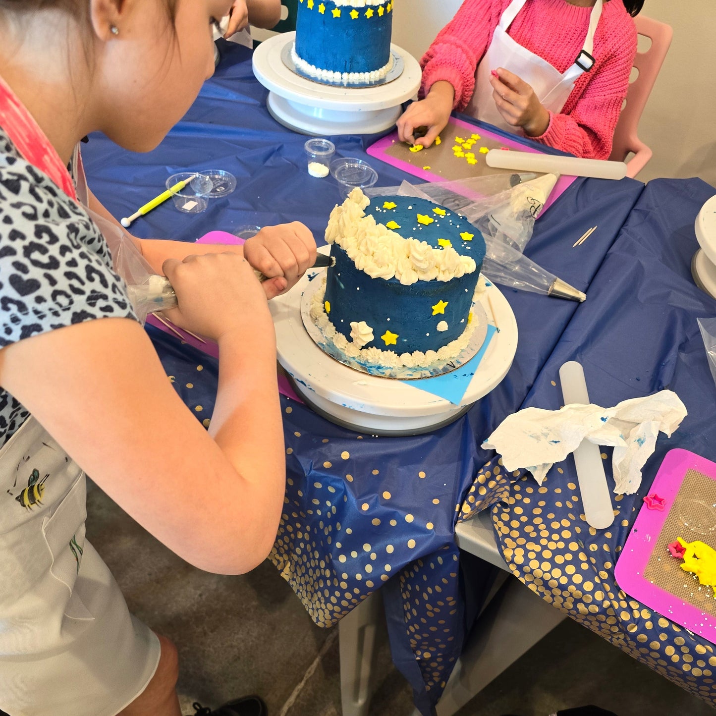 At Cake Hoopla's DIY cake/cupcake-decorating studio, a kid adds white frosting decorations to a blue cake she frosted and decorated with yellow stars.