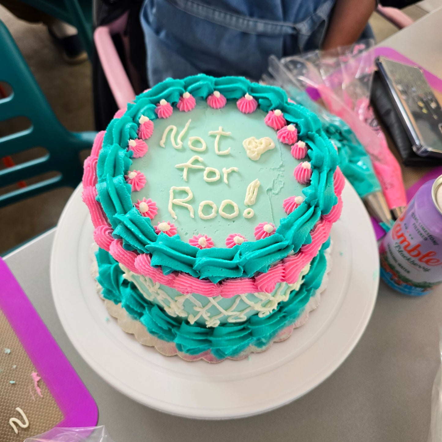 A teal, white, and pink cake decorated with piped borders, shells, and writing at Cake Hoopla in Tigard, Oregon, near Portland, during a cake-decorating class.