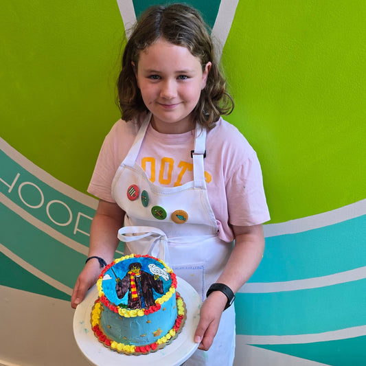 A girl shows off her Harry Potter cake with red and yellow borders made during Cake Hoopla's summer cake camp at Cake Hoopla.