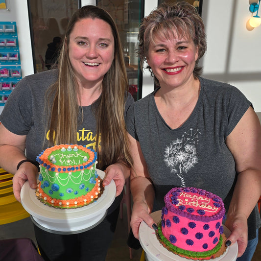Two women show off their unique cakes completed during a cake-decorating 101 class at Cake Hoopla in Tigard