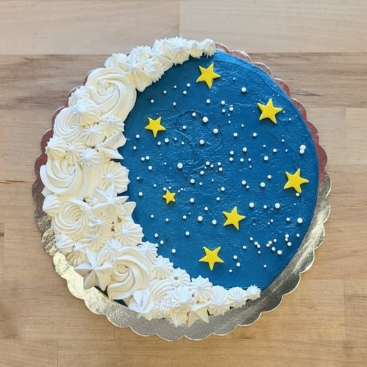 Dark blue cake with yellow stars and a white frosting crescent moon decorated at Cake Hoopla for a Cake Decorating 101 Class.