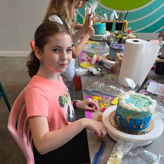 A table of kids decorates cakes, including a moon cake, at cake camp at Cake Hoopla in Tigard near Portland.