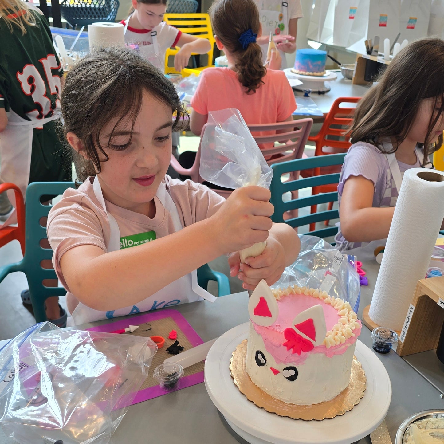 Children decorating cakes in a classroom setting with various decorating tools and ingredients at Cake Hoopla in Tigard, near Portland.
