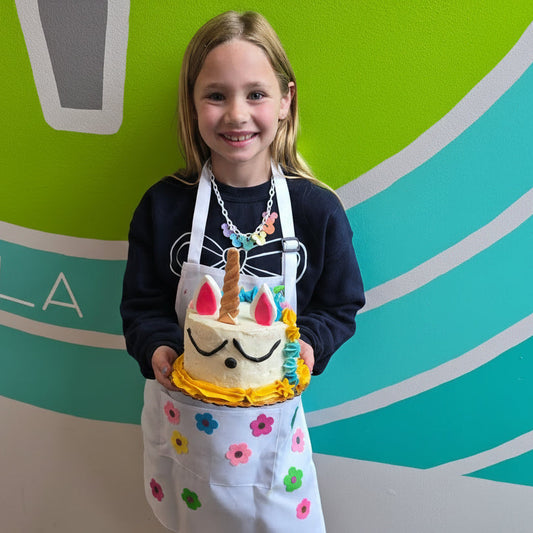 Girl holding her unicorn cake creation in front of a colorful mural at Cake Hoopla's summer cake camp.