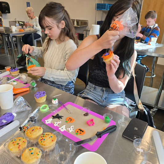 Kids decorating Halloween cupcakes during a Cake Hoopla class in a kitchen setting with various baking tools and ingredients.