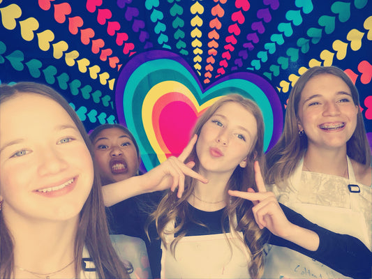 A group of girls enjoy Cake Hoopla's photo booth with a rainbow heart background during a birthday party.
