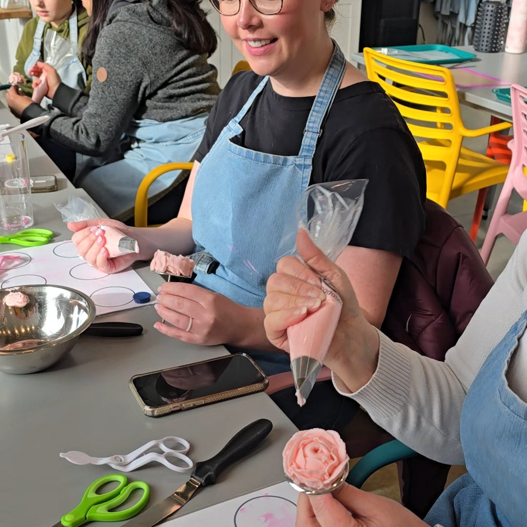 Woman pipes rose with pink buttercream on frosting nail at Cake Hoopla in Tigard, near Portland.