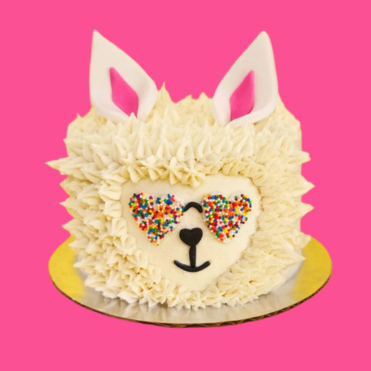 Cute llama cake with white frosting fur and heart-shaped rainbow-sprinkled sunglasses, ready to serve or decorate during open studio time or via a to-go cake kit at Cake Hoopla in Tigard, near Portland.