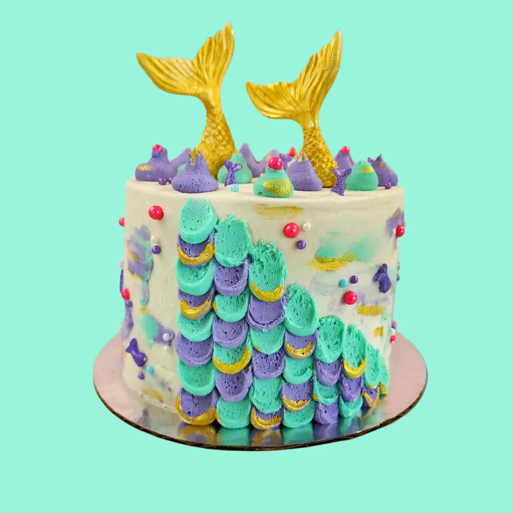 Mermaid cake with teal and purple frosting, gold mermaid tails, and pink and purple sprinkles; a pre-decorated cake shipped to the continental US.