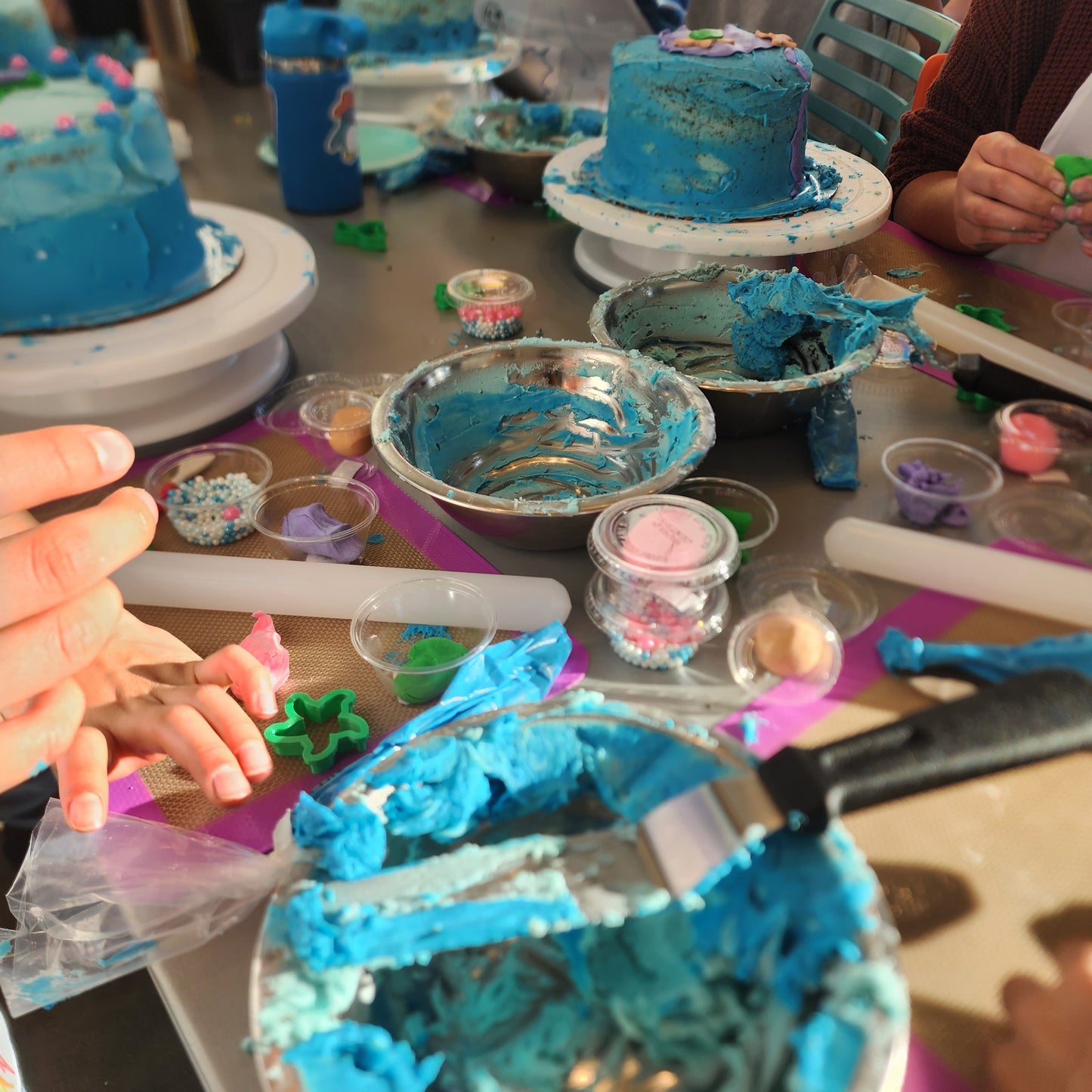 A table full of cake-decorating supplies, including ocean-blue frosting, a variety of fondants, and cakes beautifully frosted in shades of blue for an under-the-sea-themed cake-decorating party at Cake Hoopla in Tigard, near Portland.