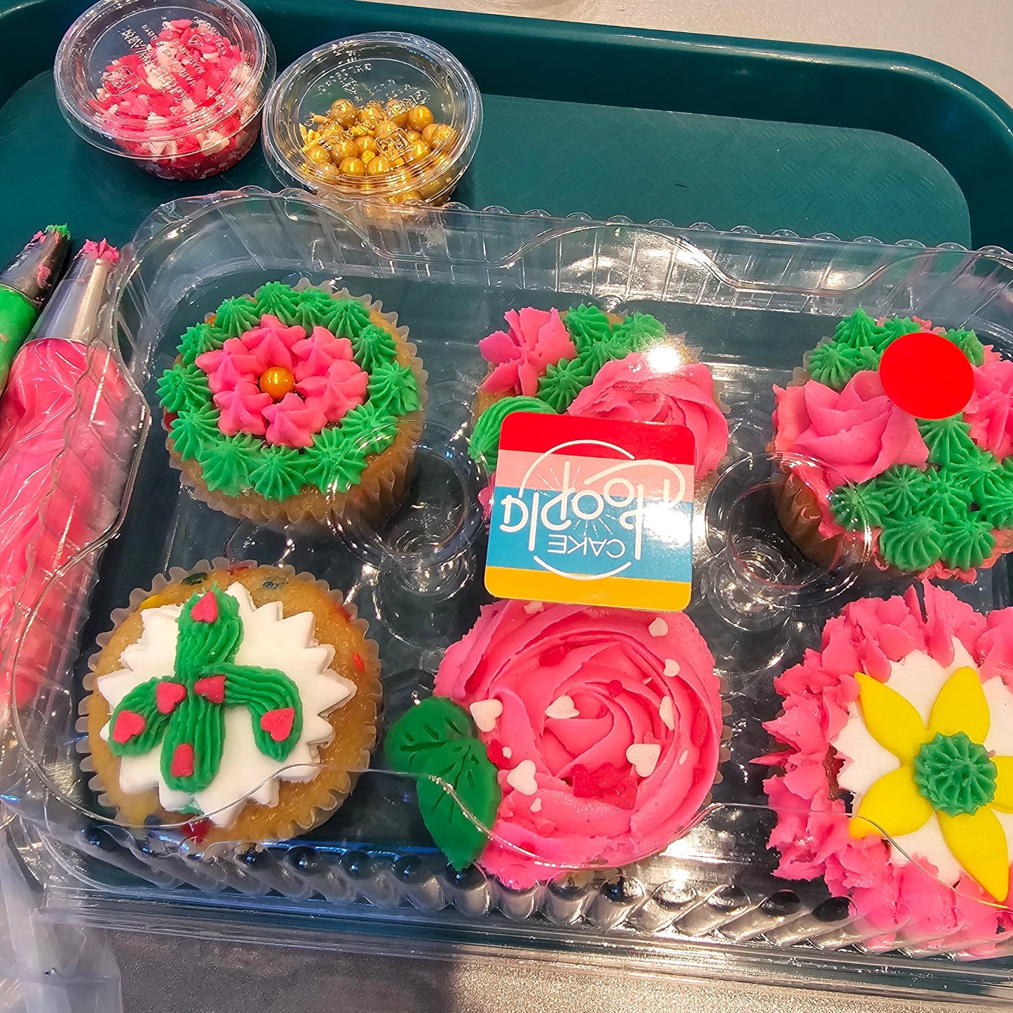 Cupcakes decorated with green and pink frosting, yellow and white fondant, and gold and hear sprinkles from the Create Your Own Cupcake Kit available during time or as a to-go kit from Cake Hoopla in Tigard, Oregon near Portland.