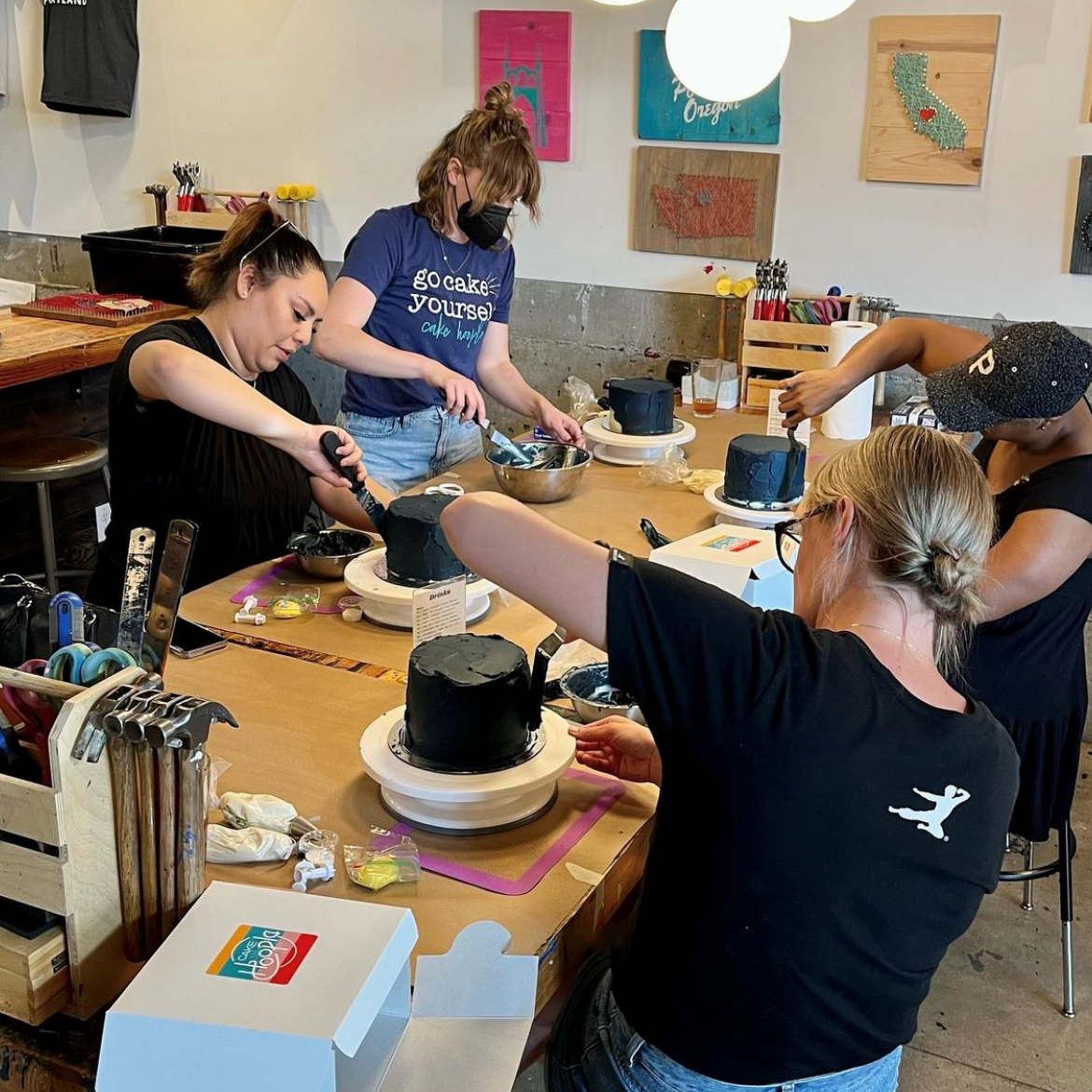 In a fun setting, four people frosting cakes with dark blue frosting.