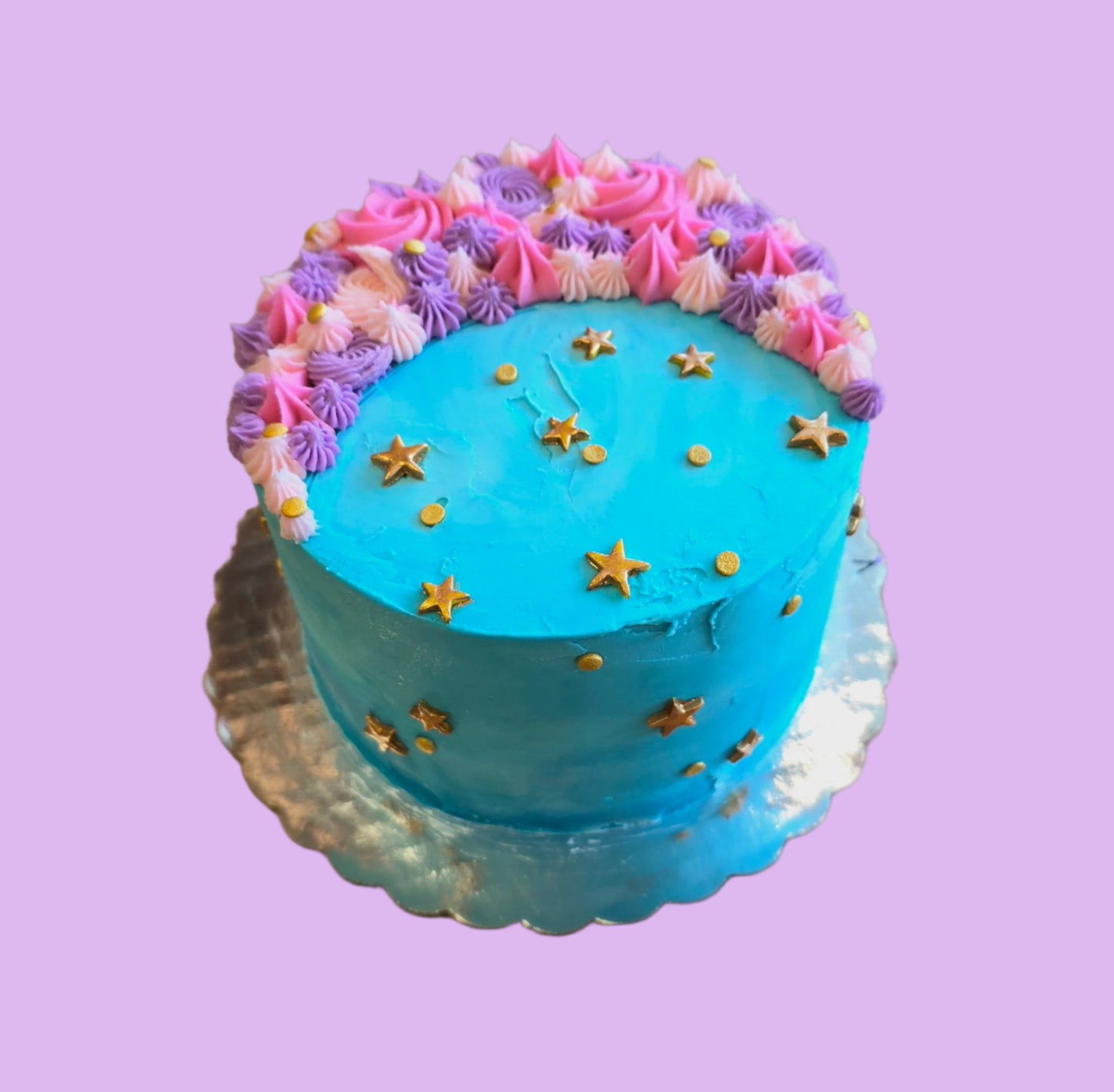 A moon-themed cake frosted in teal with pink and purple crescent moon on top and gold stars dotting the cake; a pre-decorated cake available for purchase at Cake Hoopla in Tigard, Oregon.