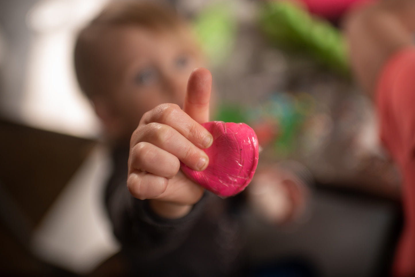 At a custom DIY cake decorating party in the Portland area, toddler is excited to show the camera a handful of pink fondant squished between her fingers. She holds it out proudly above her head.