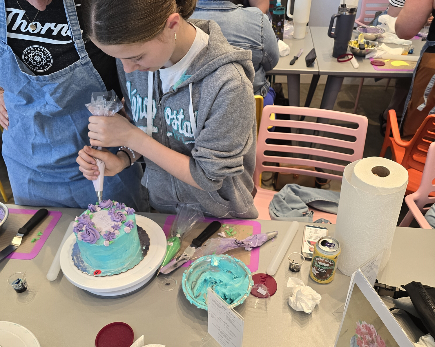 Middle school age kid decorates a cake with flowers, blue frosting, and a piping bag with tip.