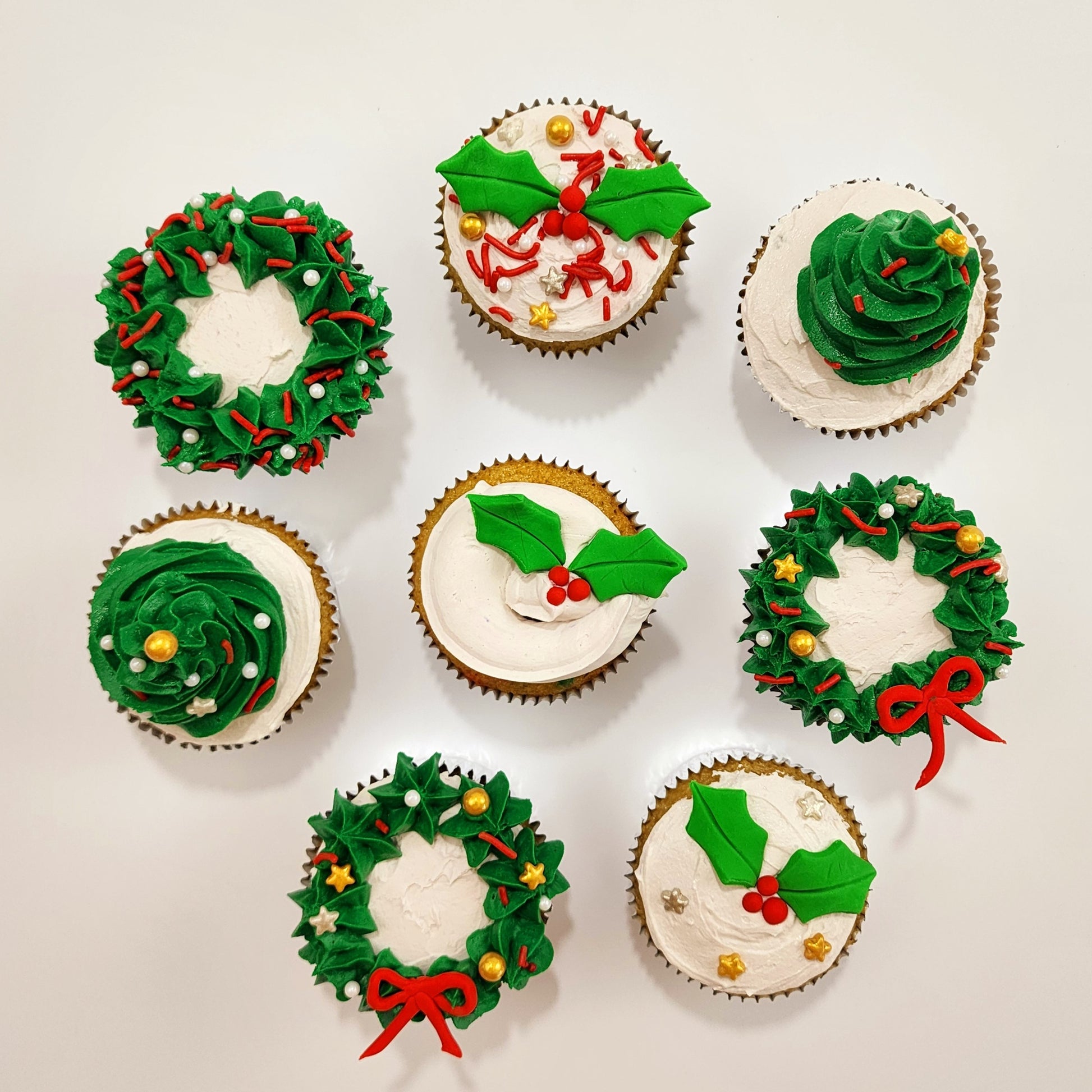 DIY cupcake decorating Christmas cupcakes with wreath and Christmas trees topping the cupcakes. Fondant holly leaves and gold, silver, and red sprinkles.