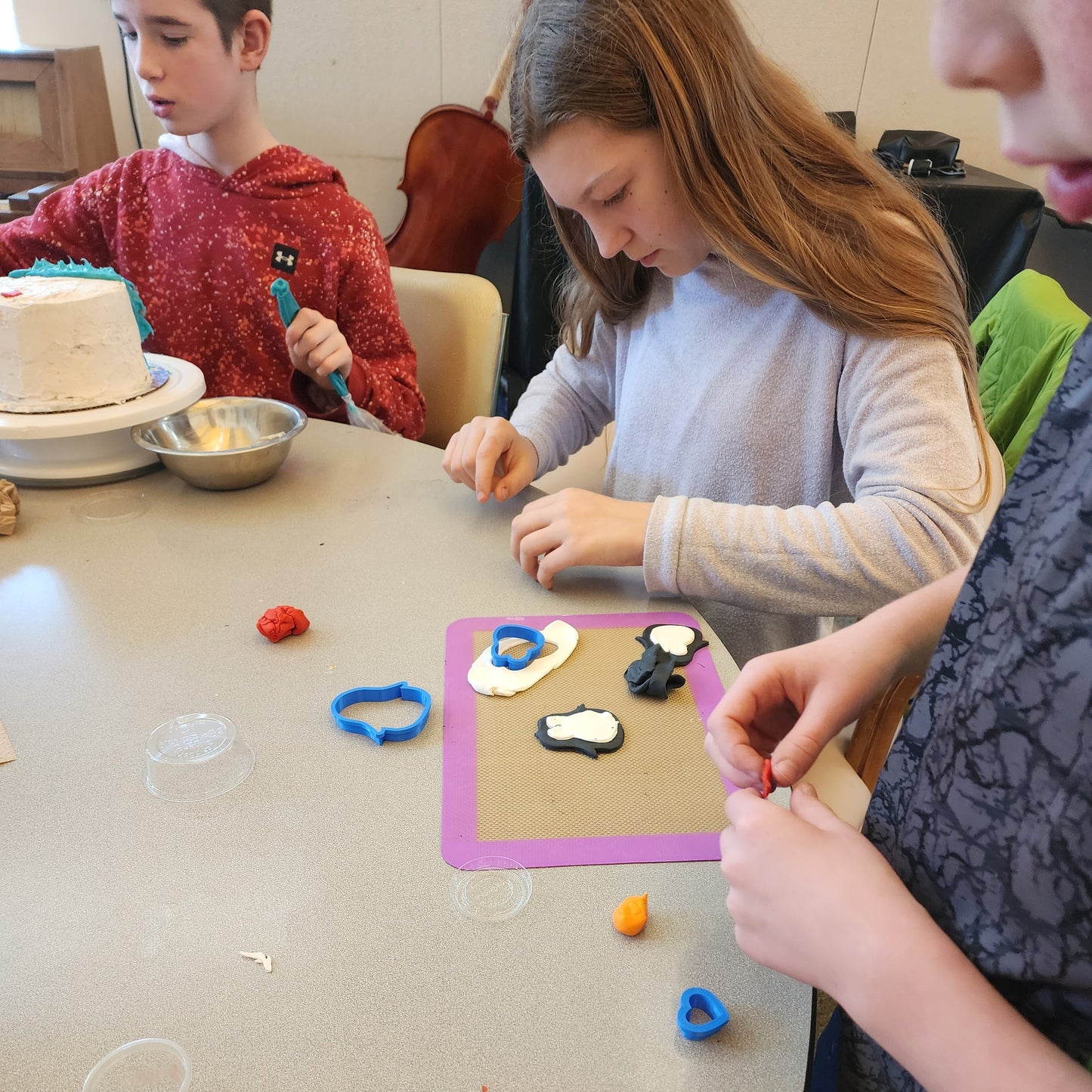 Several kids are focusing on creating fondant penguins for their penguin-themed cake at a Cake Hoopla event.