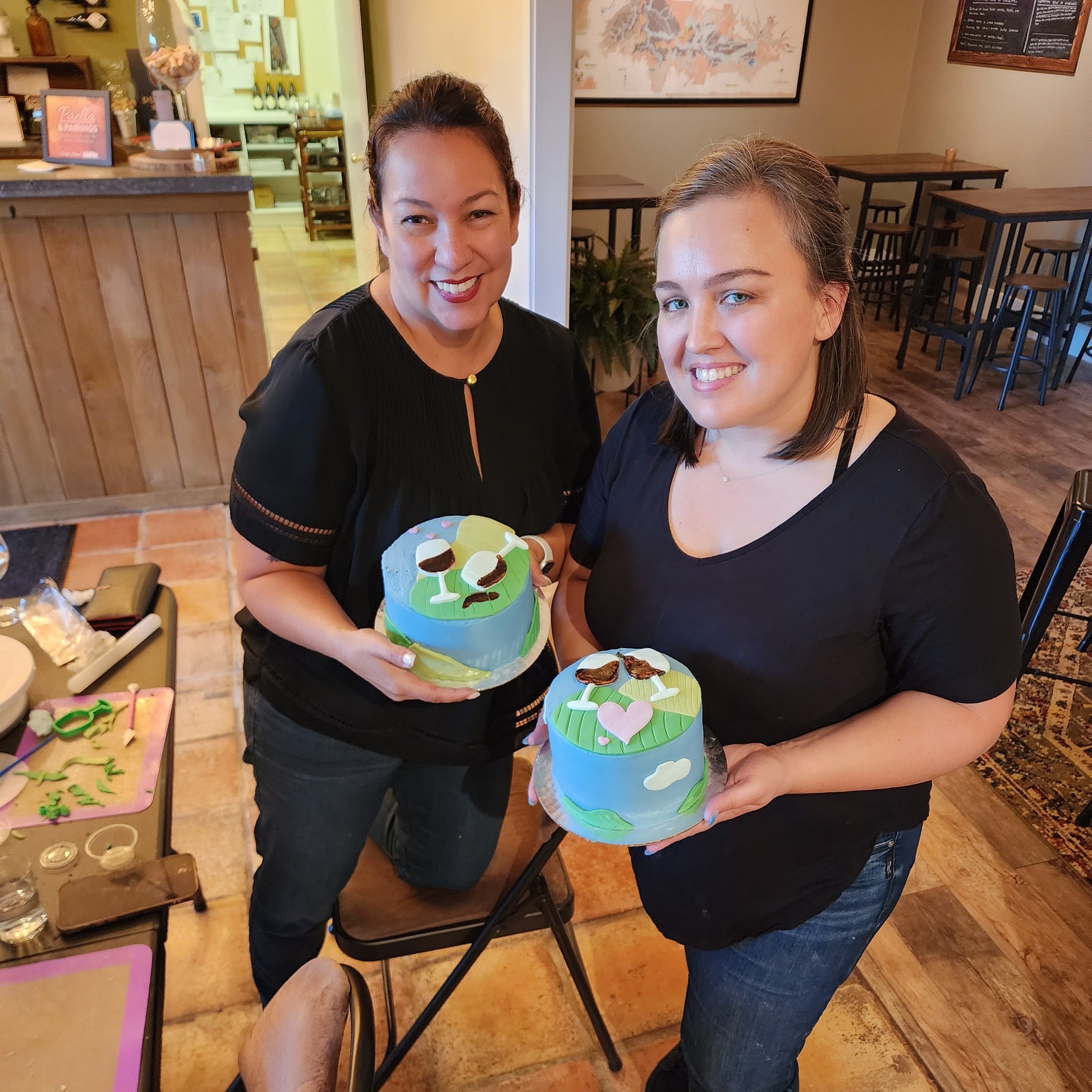 two peopel showing off their unique wine-themed cakes made during a Cake Hoopla cake-decorating workshop