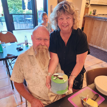 a couple shows off the cake they decorated during a wine-themed cake-decorating workshop. a happy, fun, crafty activity