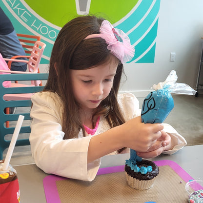 Little girl pipes frosting onto a cupcake during open studio time at Cake Hoopla in Tigard, Oregon near Portland.