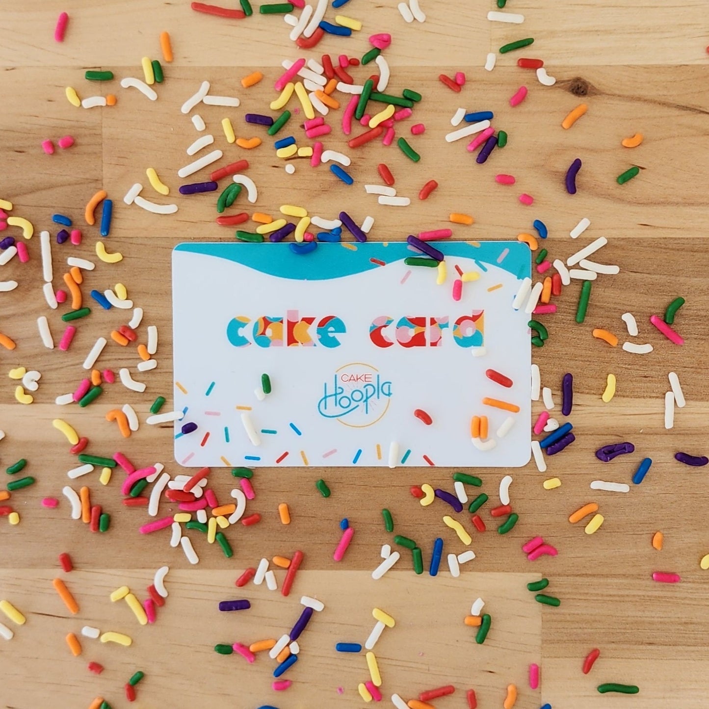 A credit-card-sized gift card to Cake Hoopla reading "cake card" adorned with colorful sprinkles.