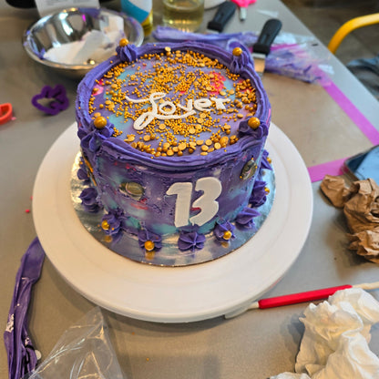 A customer at Cake Hoopla's DIY cake-decorating studio decorated their cake in blue, pink, purple, and gold to look like a famous pop star's album cover.