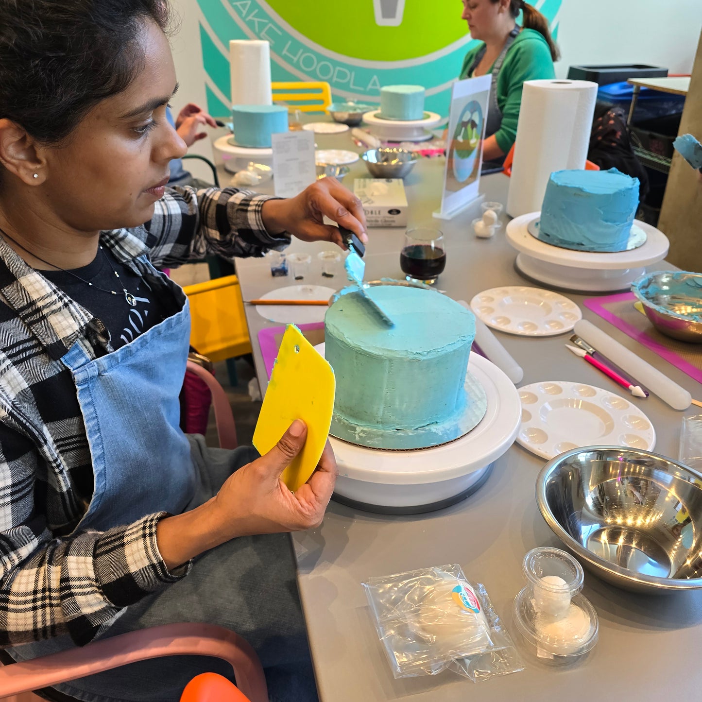 A woman decorates a cake, smoothing frosting over the top, at Cake Hoopla in the Portland area during a cake-decorating workshop.