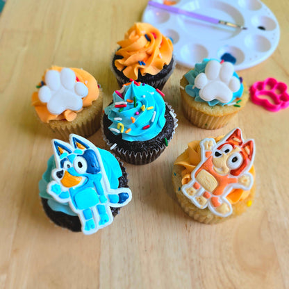 Cupcakes decorated during a DIY cupcake-decorating workshop at Cake Hoopla with blue and orange frosting, fondant dog paws, and blue and red heeler dogs who look like the cartoon characters Bluey and Bingo