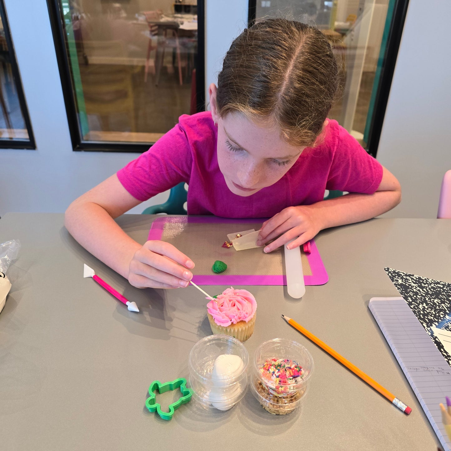 A girl concentrates on decorating a pink cupcake during open studio time at Cake Hoopla in Tigard, Oregon near Portland.