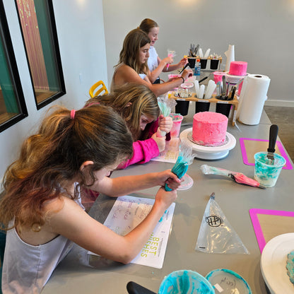 A group of kids happily decorates cakes and practice writing with frosting at a summer cake camp at Cake Hoopla in Tigard, Oregon near Portland.