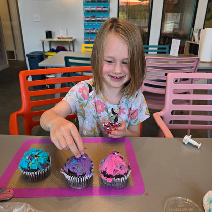 A cute girl decorates pink, blue, and purple cupcakes and tops them with sprinkles at Cake Hoopla in Tigard, Oregon near Portland.