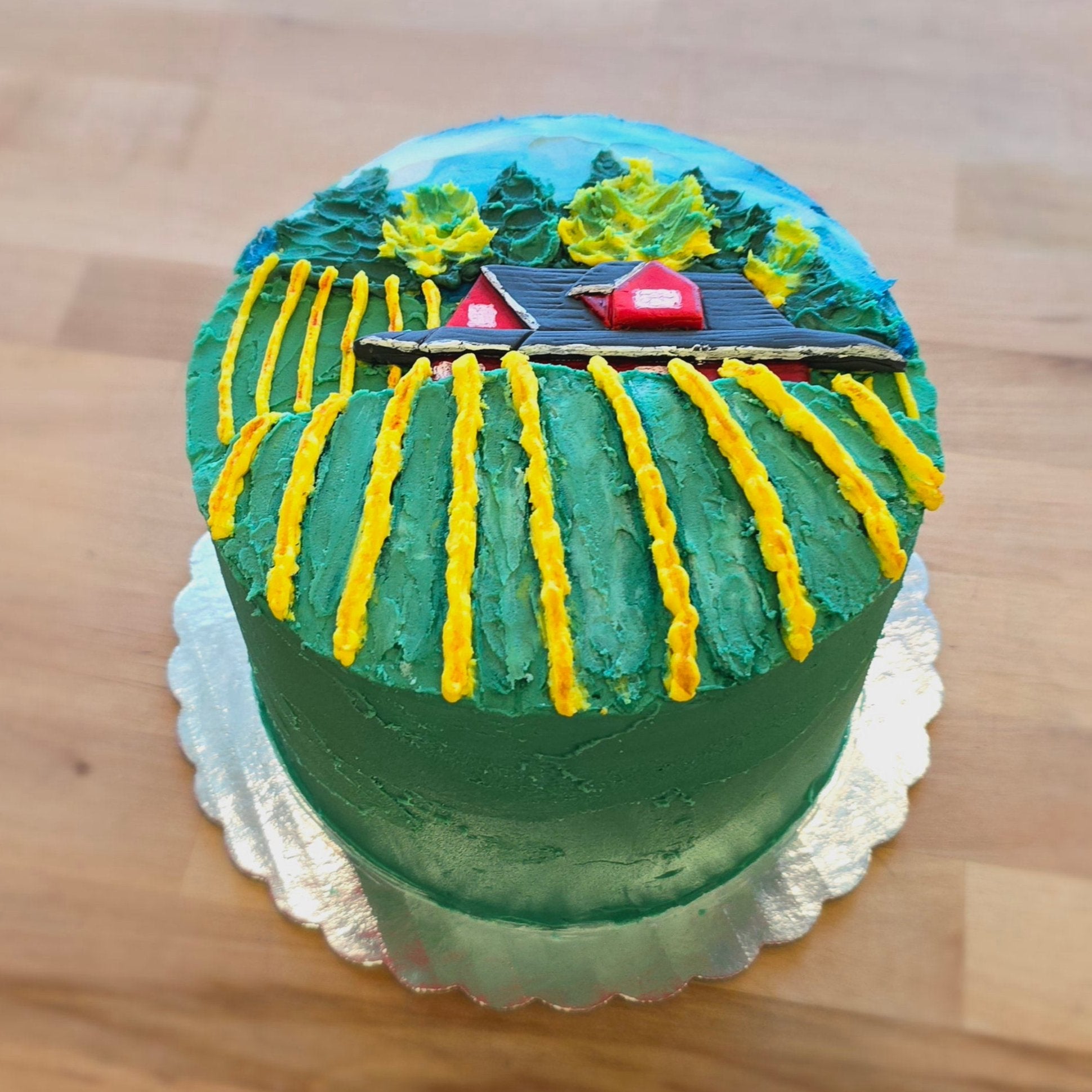 Round cake decorated like a vineyard in the fall, with yellow rows of grapes, the Sokol Blosser red house, and trees in the skyline. 