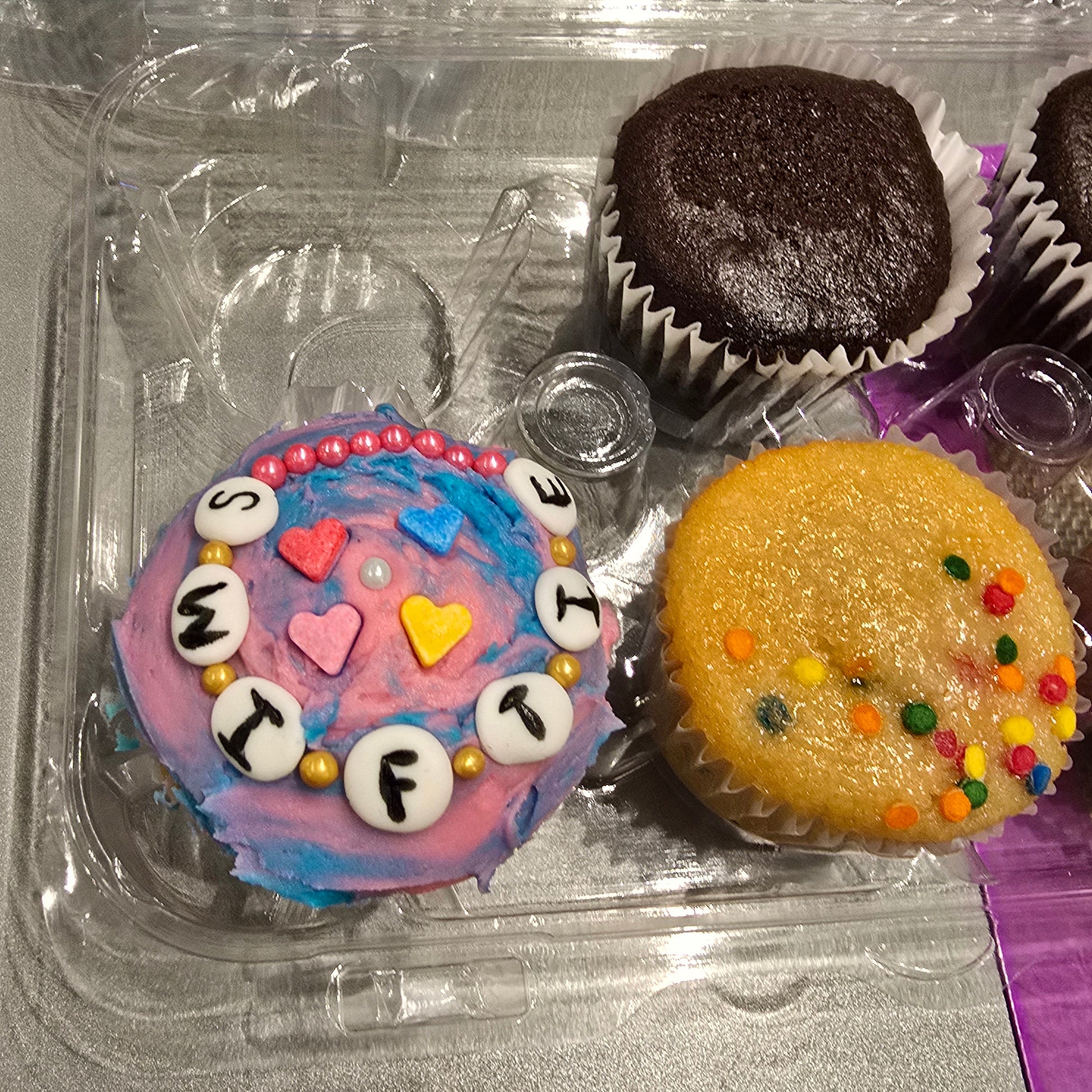 A Cake Hoopla customer's DIY Swiftie-themed Friendship Bracelet cupcakes, one decorated saying "Swiftie" and two undecorated, during open studio time in Tigard, Oregon, near Portland.