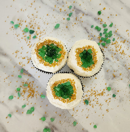 Geode cupcakes frosted white with green candy gems in the middle surrounded by gold sprinkles; pre-decorated cupcakes available for pick up at Cake Hoopla in Tigard, Oregon, in the Portland area.