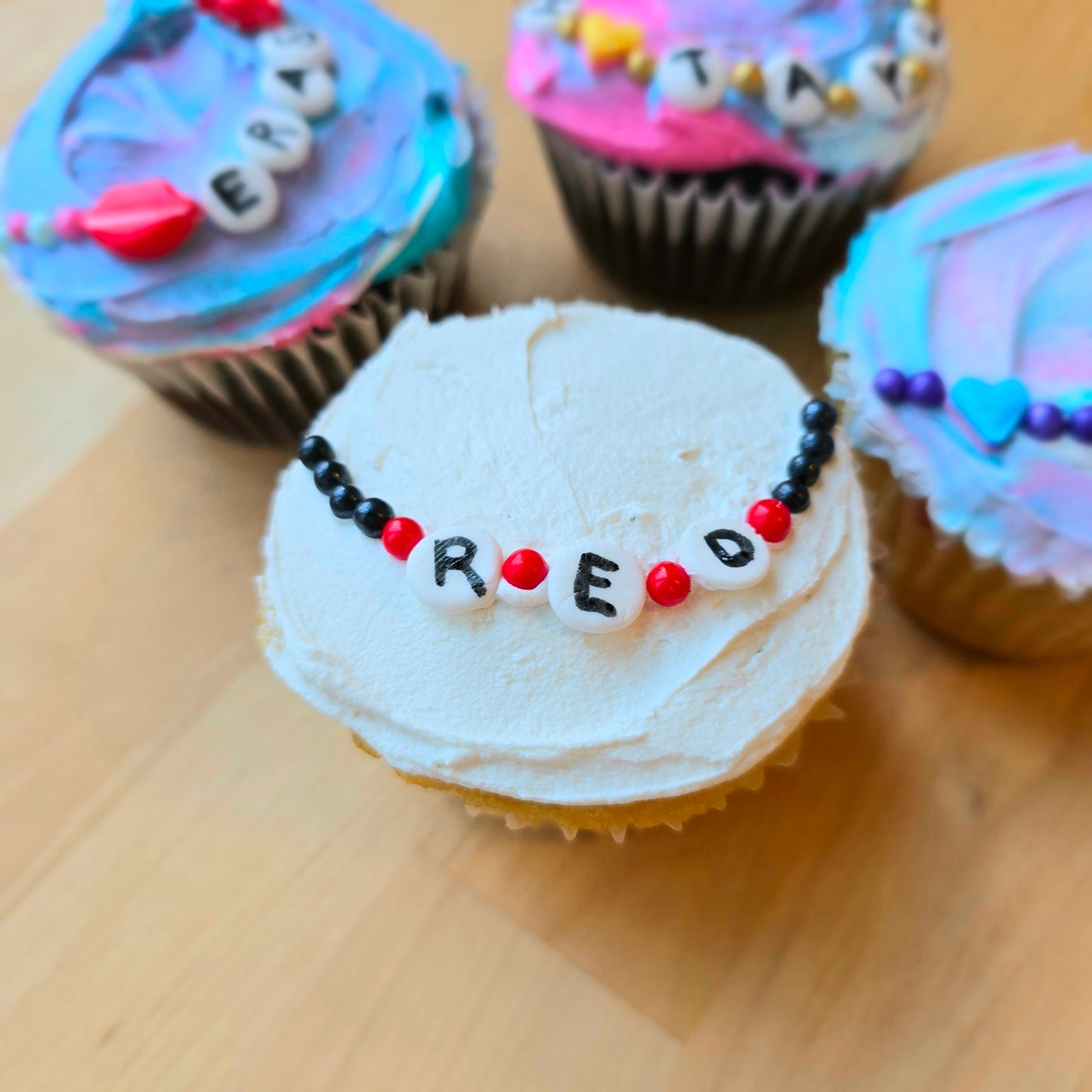 Friendship-bracelet-themed cupcake decorated at Cake Hoopla in Tigard, Oregon near Portland as a DIY cupcake-decorating kit, with the word "RED" written on it.