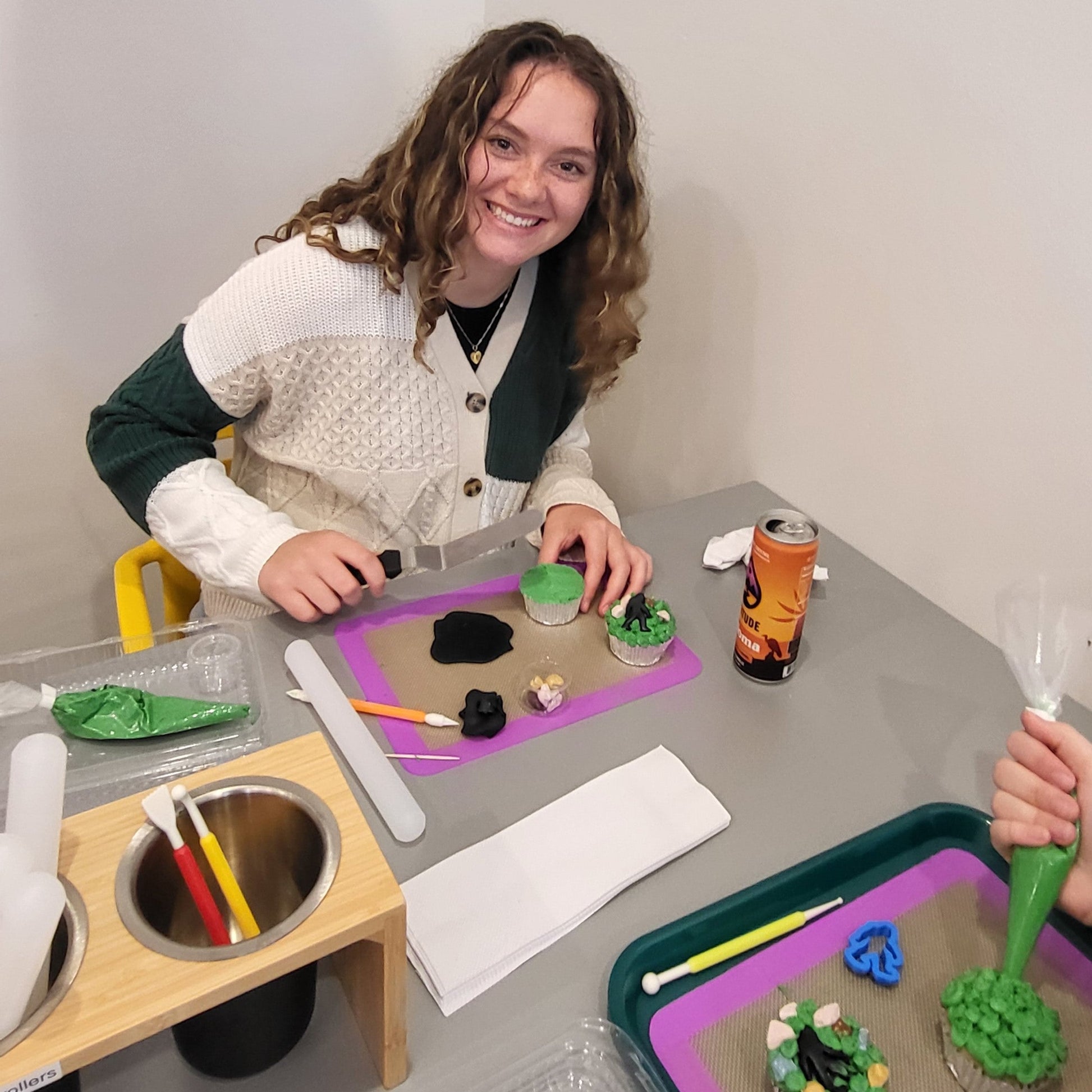 A young adult customer decorates cupcakes with green frosting and a black fondant bigfoot at Cake Hoopla's DIY cake/cupcake-decorating studio in Tigard, near Portland.