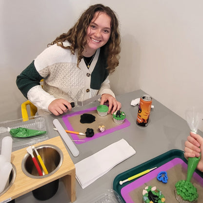 A young adult customer decorates cupcakes with green frosting and a black fondant bigfoot at Cake Hoopla's DIY cake/cupcake-decorating studio in Tigard, near Portland.