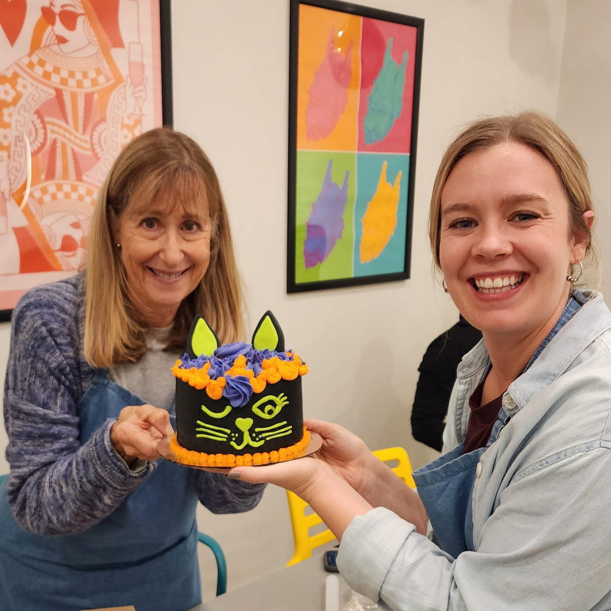 Two women show off their Halloween black cat cake they decorated at Cake Hoopla in Tigard, near Portland.