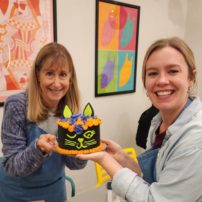 Two women show off their Halloween black cat cake they decorated at Cake Hoopla in Tigard, near Portland.