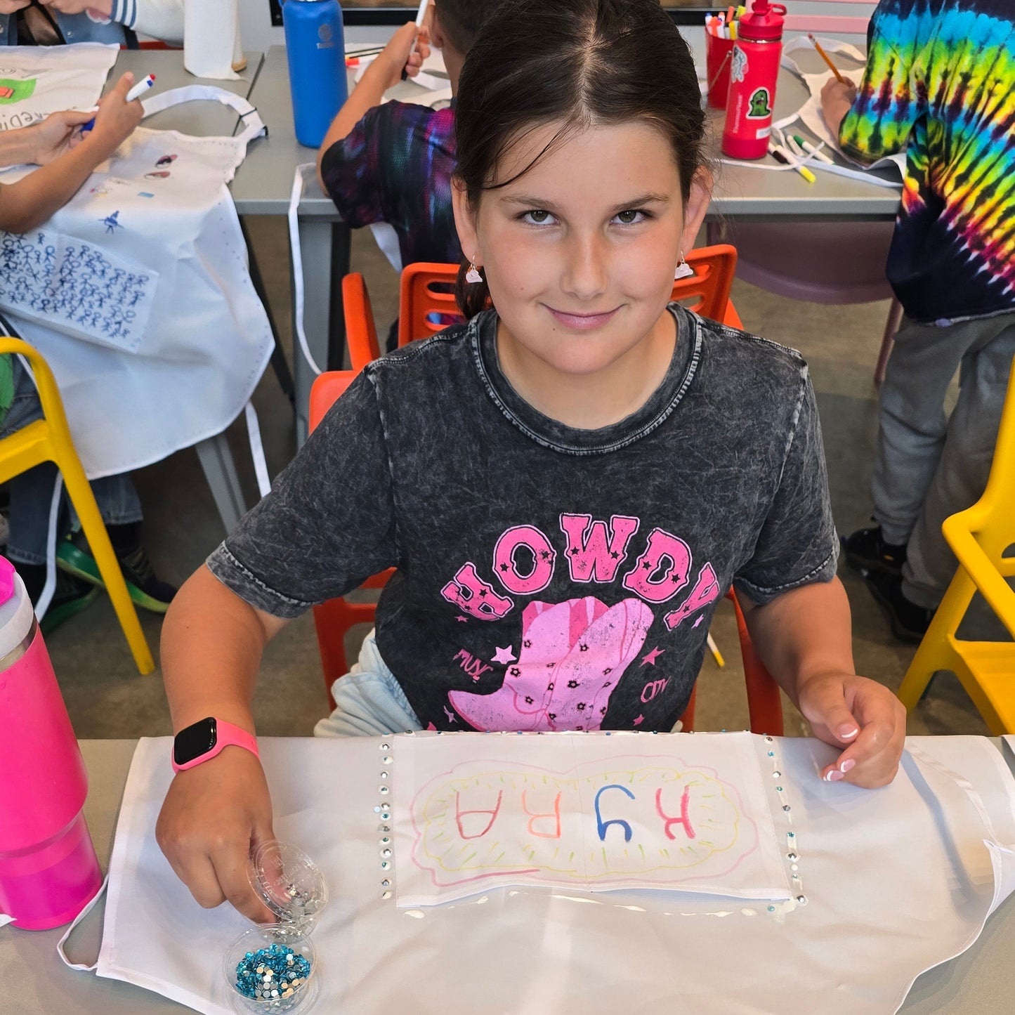 Girl decorates white apron at Cake Hoopla with colorful markers.