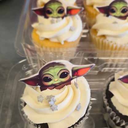 Frosted cupcakes topped with a small Star Wars Grogu/Baby Yoda topper, arranged in a clear plastic cupcake tray.