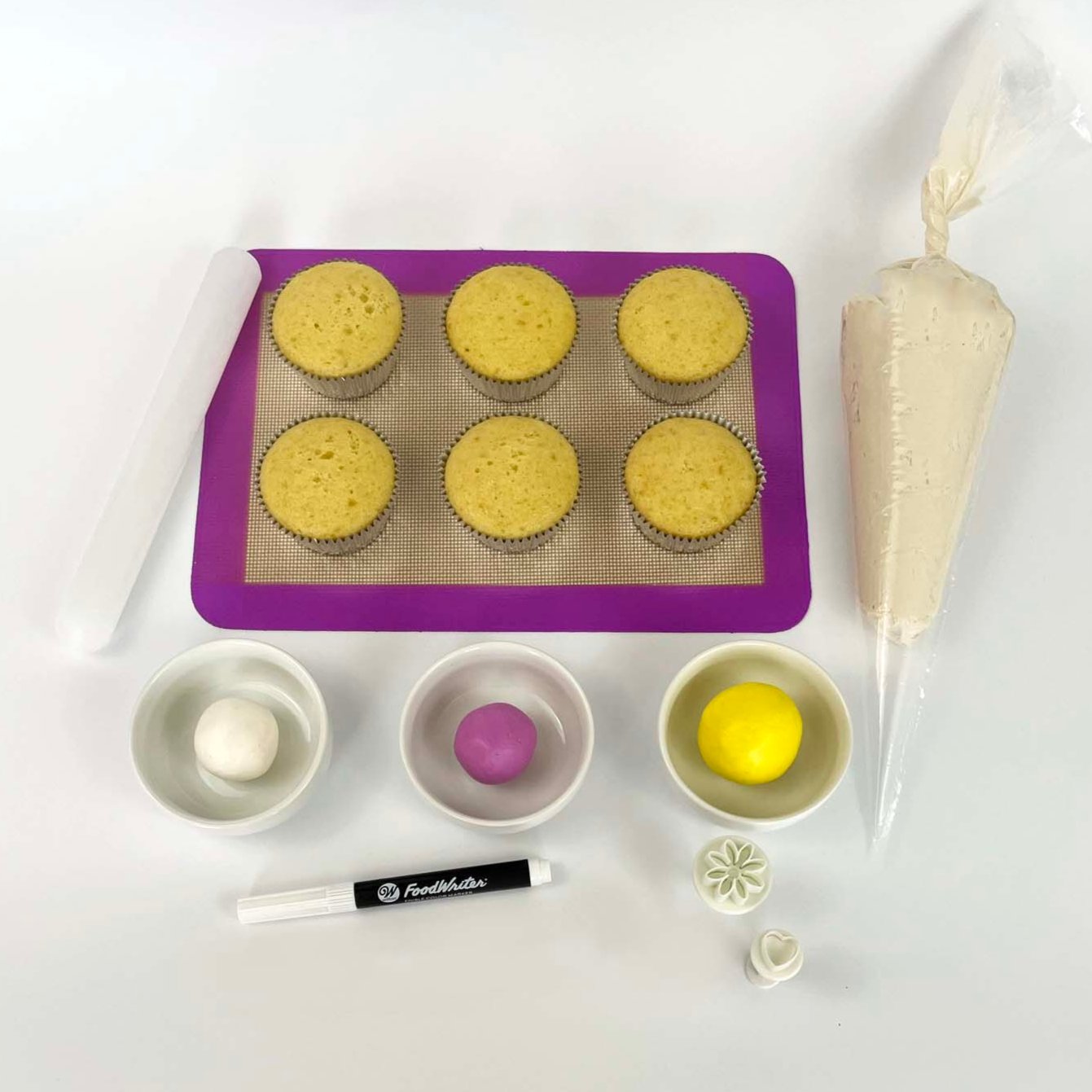 Picture of DIY bee-themed cupcake-decorating kit with white buttercream frosting, pink, yellow, and white fondant, black edible marker, and fondant cutters for use at Cake Hoopla's open studio time in Tigard, Oregon.