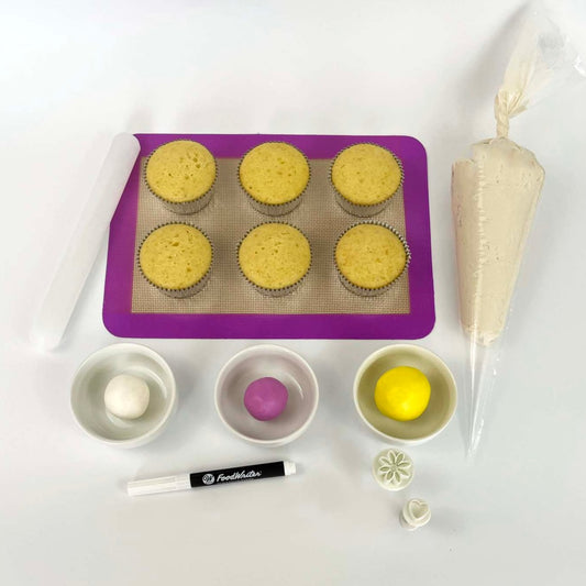 Picture of DIY bee-themed cupcake-decorating kit with white buttercream frosting, pink, yellow, and white fondant, black edible marker, and fondant cutters for use at Cake Hoopla's open studio time in Tigard, Oregon.