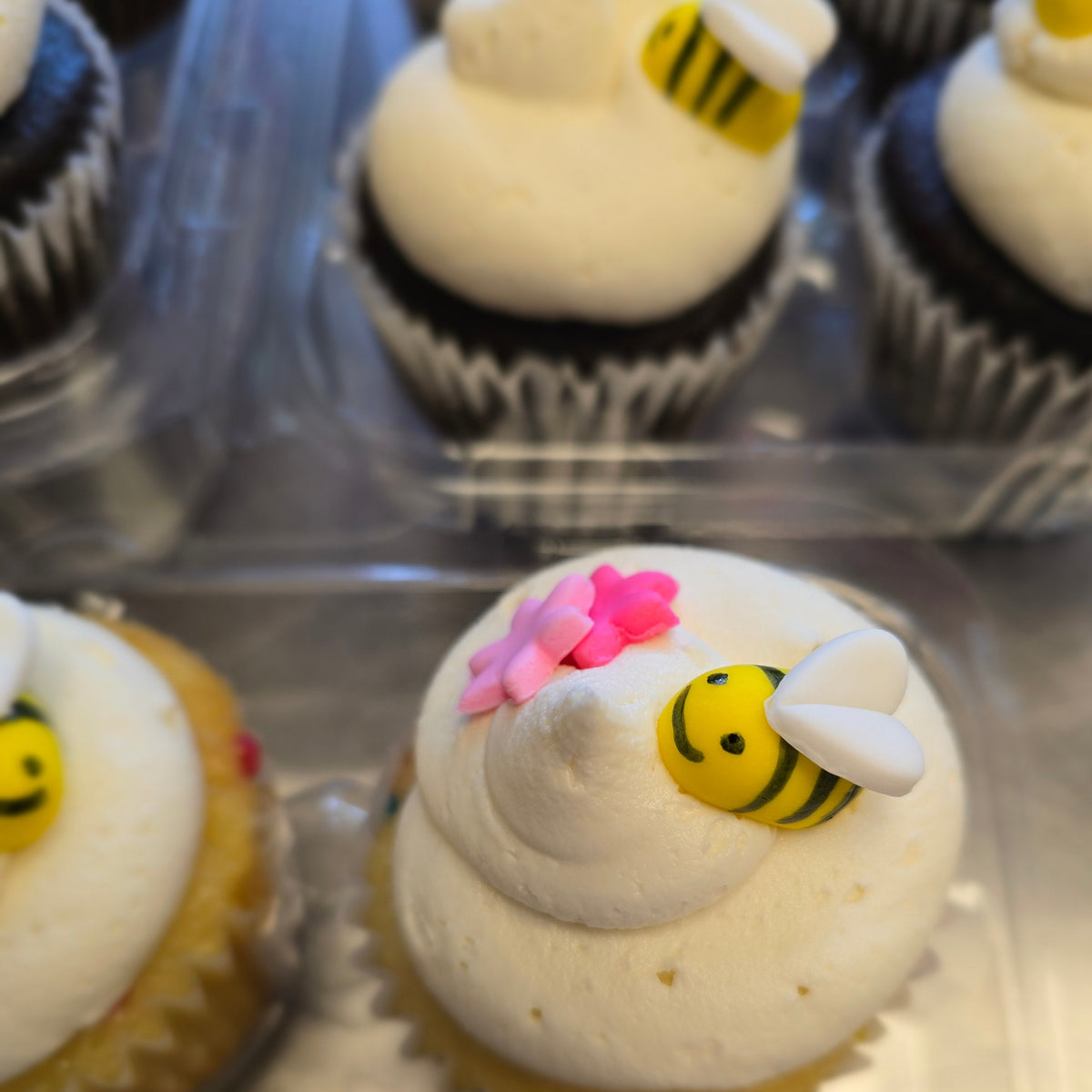 Fondant bee and two pink flowers on top of a white frosted vanilla cupcake.