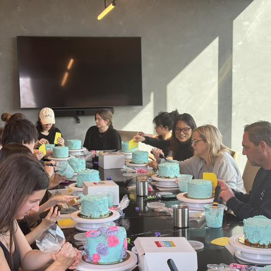 A group of adults decorates cakes in a boardroom setting in Portland, Oregon