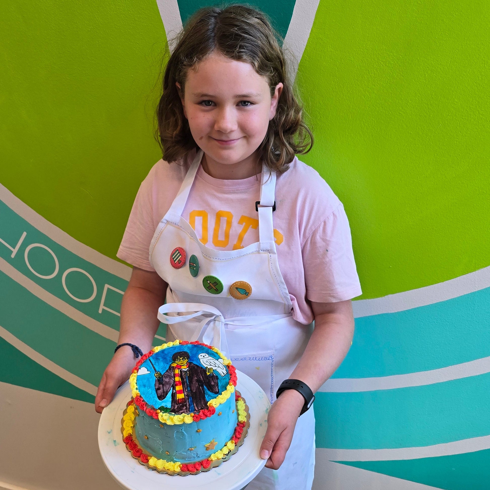 A girl shows off her Harry Potter cake with red and yellow borders made during Cake Hoopla's summer cake camp at Cake Hoopla.