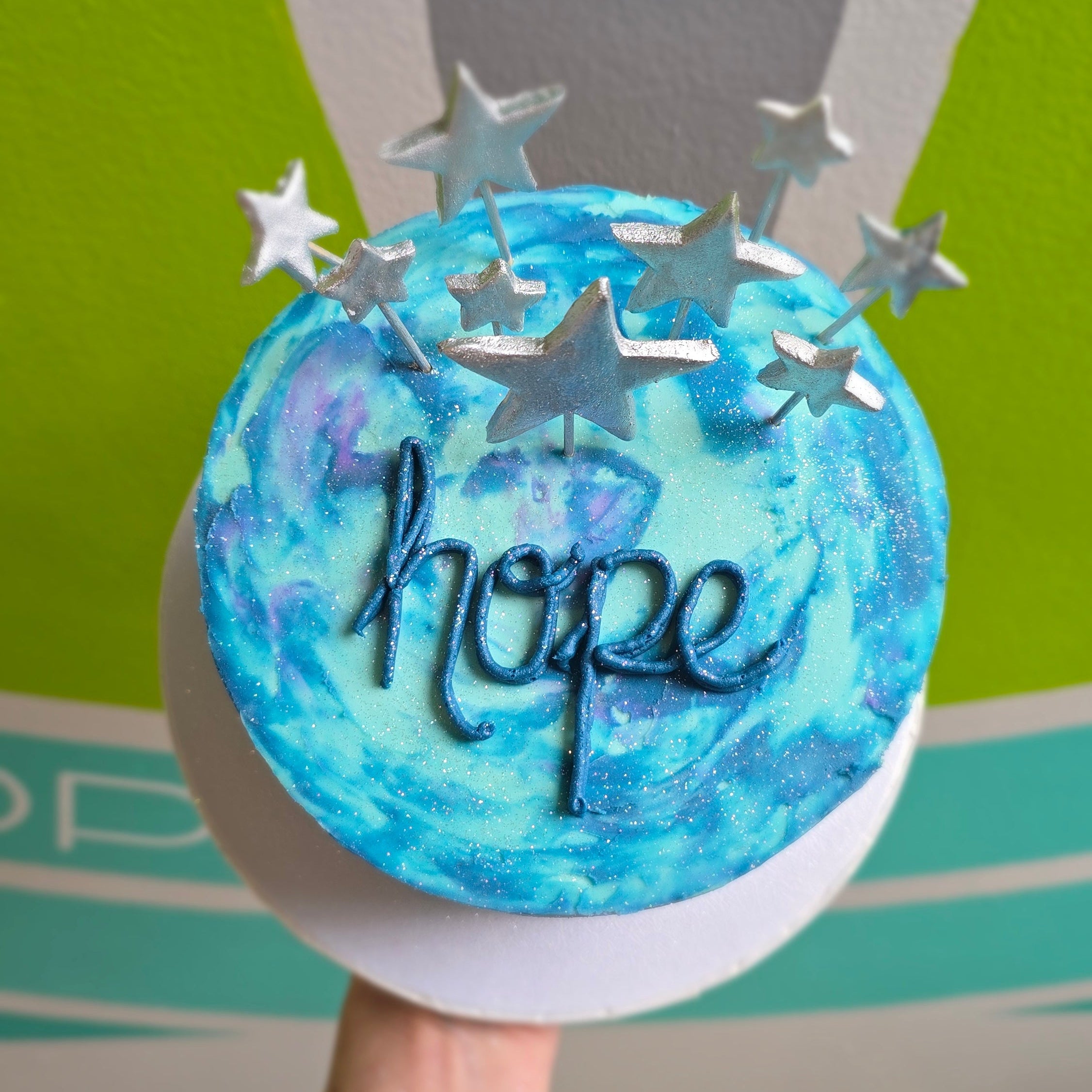 Celestial blue cake with swirls, silver stars, and the word "hope" written on top.