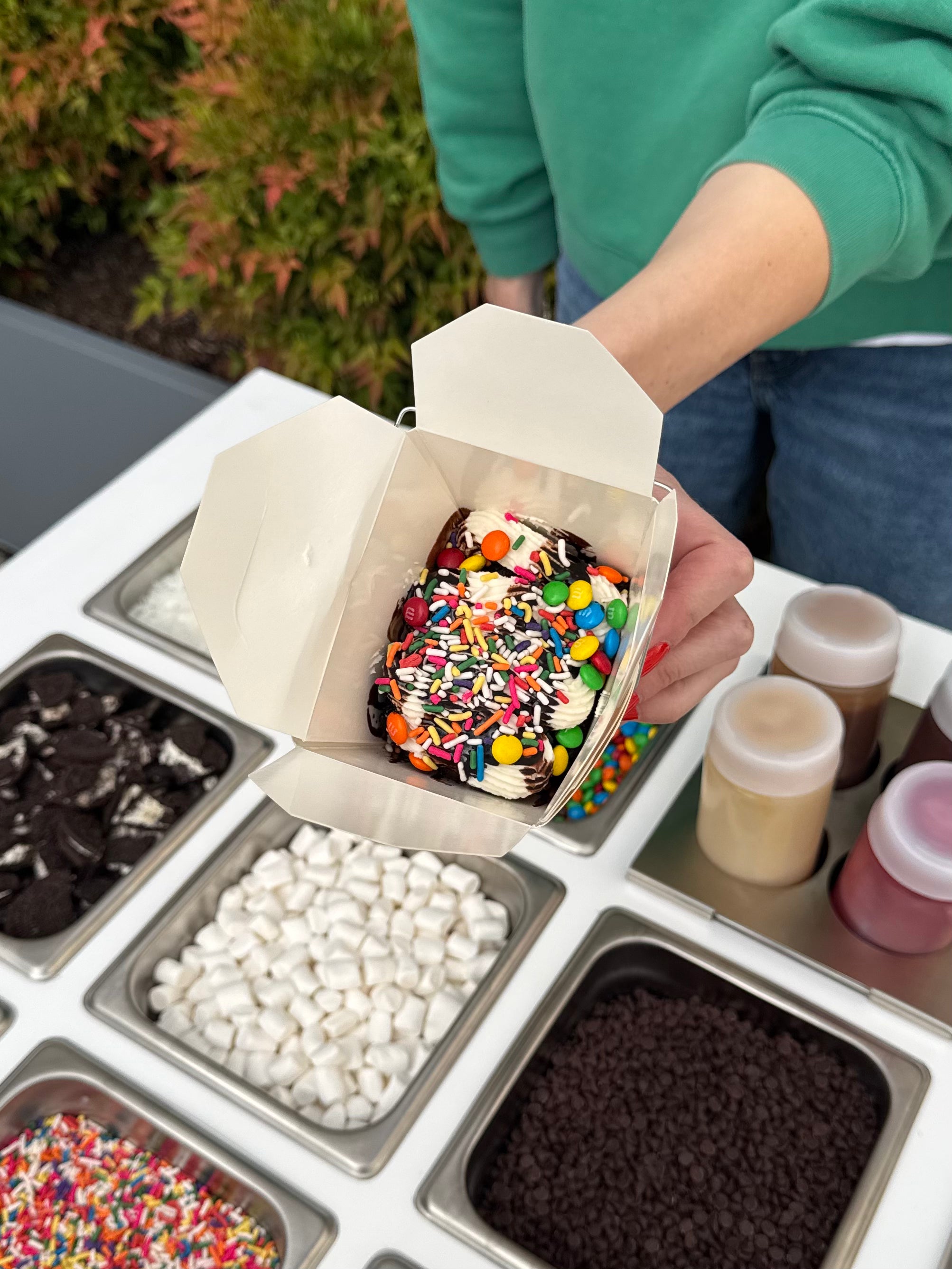 Guest holding colorful cake box filled with cake, frosting, sprinkles, and candy in handy to-go box at a Portland Cake Cart event.