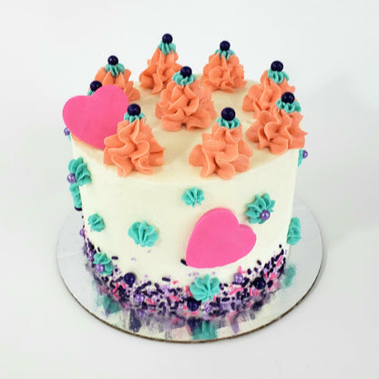 A bright, springtime array of colors on a white frosted cake. Teal frosting stars dot the sides of the cake, mounds of peach-colored frosting circle the top of the cake, and a purple sprinkle mix lines the bottom of the cake. One bright pink fondant heart rests against a frosting mound on top of the cake, and one is pressed into the frosting on the side of the cake. Available for shipping to the continental US.