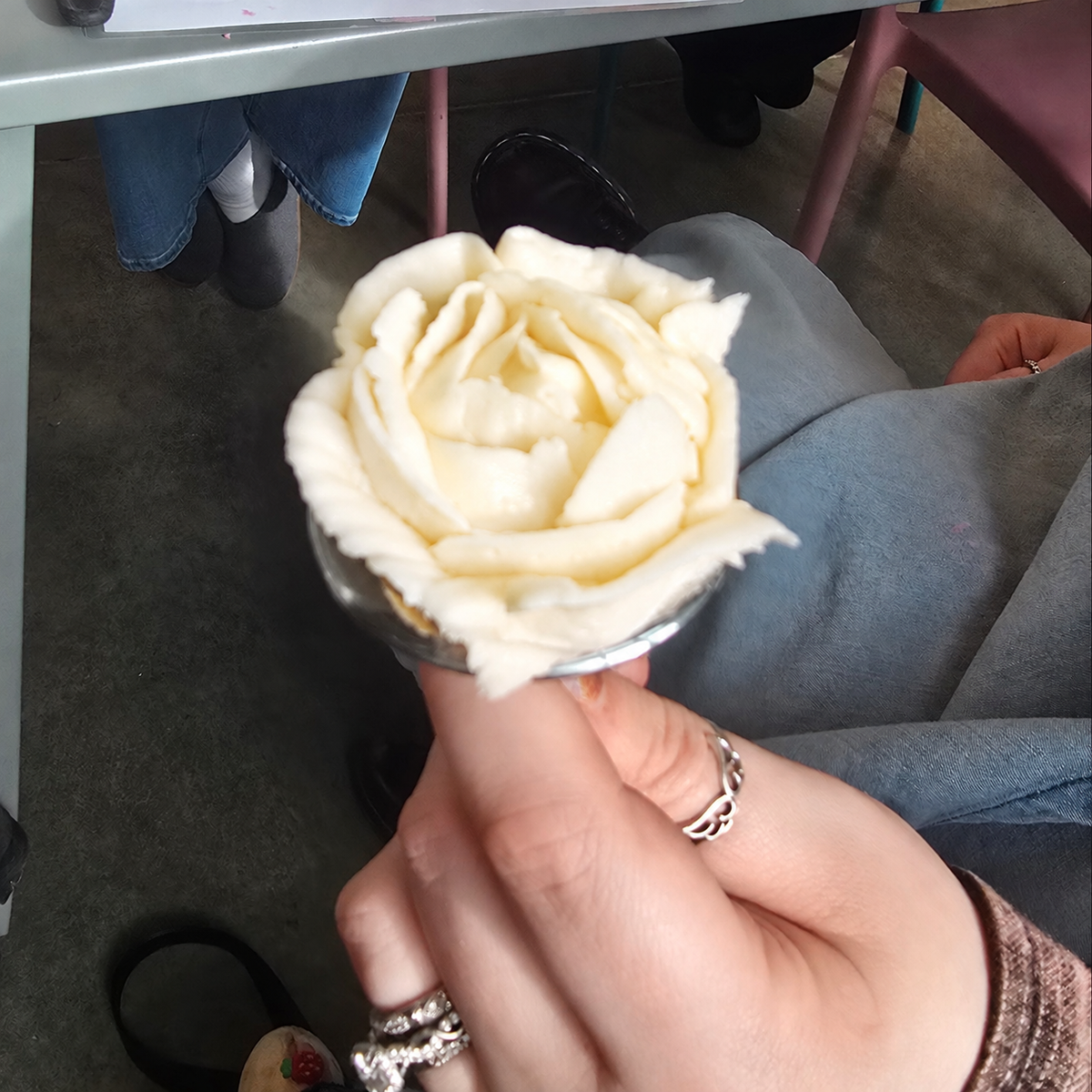 White frosting rose held on a frosting nail by a closeup hand.